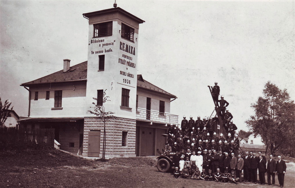 Budynek OSP w Suchej Górnej z 1936 r., przed którym pozują strażacy. Fotografia w zbiorach NAC, ta sama fotografia została opublikowana w „Przewodniku Strażackim” 