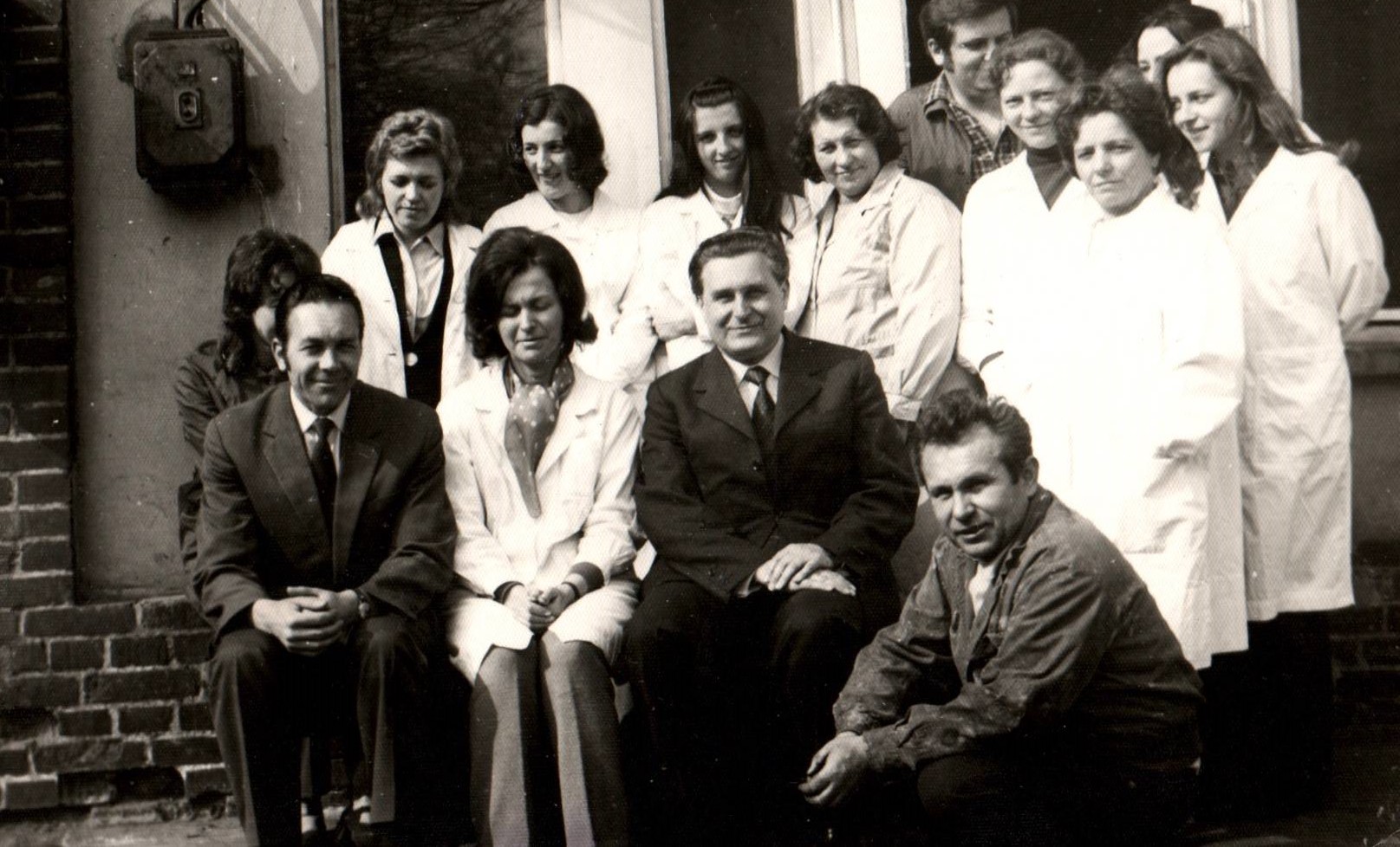 Grupa osób pozujących do zdjęcia. Część osób ma na sobie białe fartuchy. Zdjęćie stare, czarno-białe.