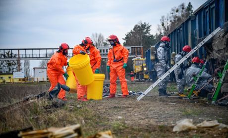 Kilku strażaków w ubraniach ochronnych prowadzi działania związane z usuwaniem substancji agresywnych.