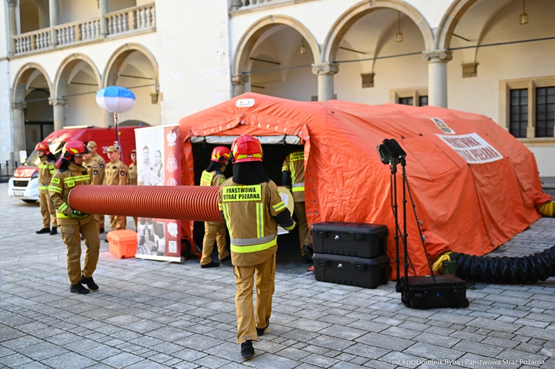 Zdjęcie z warszatów. Na zdjęciu widać duży pomarańczowy namiot. Strażacy prowadzą pokazy.