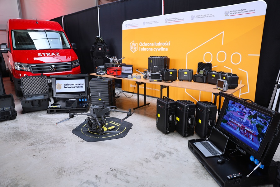 Wystawa sprzętu specjalistycznego. Na stole leżą czarne walizki ze sprzęętem. Na podłodze stoi dron.