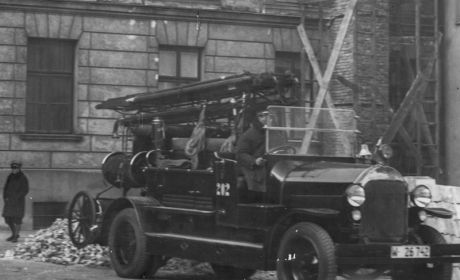 Samochód strażacki o numerze bocznym 202 w czasie akcji ratowniczej, 1932 r. / fot. NAC Czarno-białe stare zdjęcie. Samochód strażacki stoi przed budynkiem. Trwa akcja gasnicza.