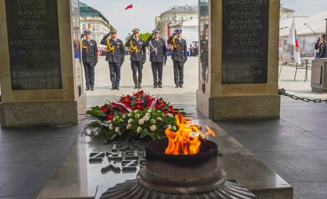 Delegacja strażaków składa kwiaty na Grobie Nieznanego Żołnierza. Na Grobie leży wieniec z biało-czerwonych kwiatów. Obok wieńca widać palący się znicz.