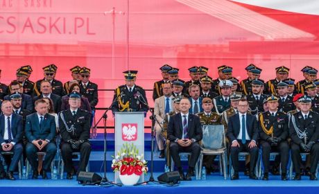 Trybuna honorowa. Zaproszeni na uroczystość goście siedzą. Przy mównicy stoi Komendant Główny PSP i przemawia do zgromadzonych osób. 