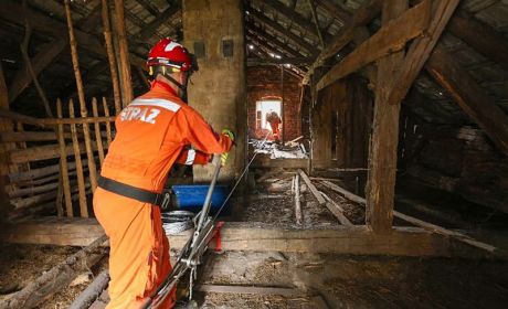 Wyciągarka ręczna i stalowa lina są niezbędnymi elementami stabilizacji w postaci ankrowania fot. mł. ogn. Kamil Nadolski Strażak w pomarańczowym ubraniu obsługuje ręczną wyciagarkę.